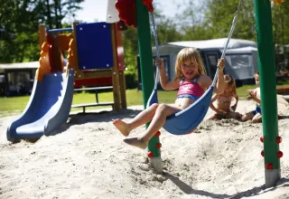 Enfants jouant sur une aire de jeux sablonneuse avec balançoires et toboggan au parc ’t Strandheem.