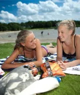 Due ragazze giovani si rilassano sui teli accanto al lago nel parco vacanze ’t Strandheem a Groningen, Olanda.