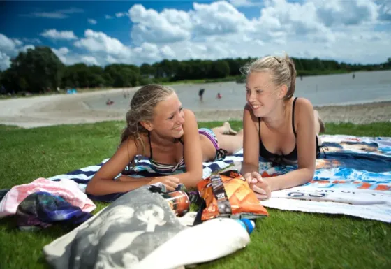 Deux jeunes filles se détendent sur des serviettes près du lac au parc de vacances ’t Strandheem, Groningen.