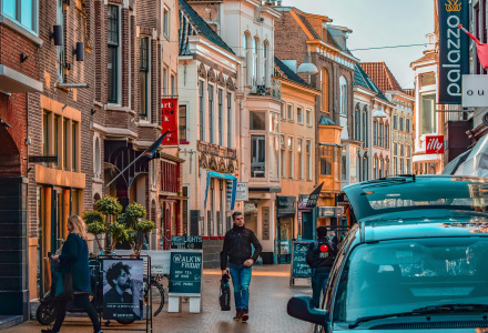 Vivace via vicino a Opende, Groningen, Paesi Bassi, con negozi, pedoni, auto e bandiera olandese.