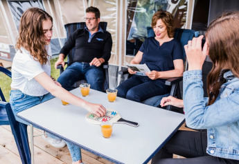 Una famiglia si diverte in una tenda safari, gioca a un gioco da tavolo e beve succo insieme seduta fuori.