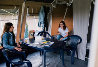 Twee vrouwen relaxen in een safaritent met plastieken stoelen, wijn en tijdschriften op tafel.