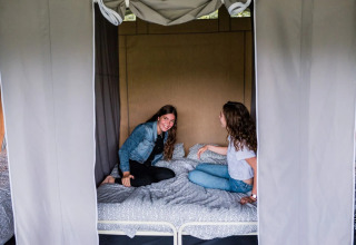 Due donne sedute conversano su un letto all’interno di una tenda safari, con tende aperte e atmosfera accogliente.