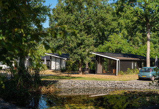 Holiday cabins and a car near a pond at Bospark Markelo, surrounded by lush trees in Overijssel, Netherlands.