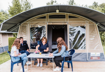 Vier personen zitten voor een safaritent, genieten van drankjes en samen zijn buiten in de natuur.