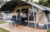 Eine Familie entspannt sich gemeinsam in einem Safarizelt mit Stühlen und Tisch auf einer Holzterrasse.