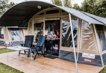 Una famiglia si gode il tempo insieme in una tenda safari, con sedie e tavolo su una terrazza di legno esterna.