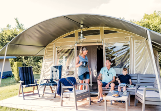 Familia disfruta de un día soleado afuera de una tienda safari, con muebles y bebidas en la terraza.