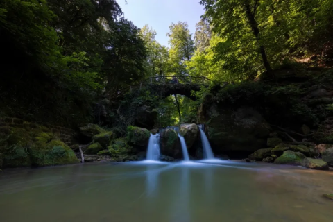 Tranquilla cascata e ponte ad arco nella foresta a Camping Gritt, Diekirch, Lussemburgo.