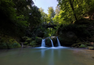 Tranquilla cascata e ponte ad arco nella foresta a Camping Gritt, Diekirch, Lussemburgo.