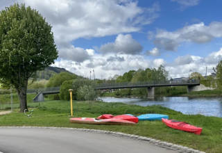 Des kayaks sur l’herbe au bord de la rivière avec un pont à Camping Gritt, Diekirch, Luxembourg.
