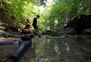 Eine Person überquert einen Bach bei Camping Gritt im Wald von Diekirch, Luxemburg, umgeben von Felsen.