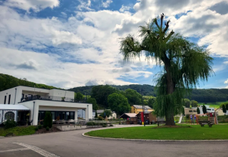 Camping Gritt holiday park in Diekirch, Luxembourg, with modern buildings, a large tree and a playground.
