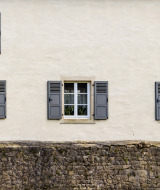 Facciata con quattro finestre e persiane grigie sopra un muro di pietra, vicino a Ingeldorf Erpeldingen, Diekirch, Lussemburgo.