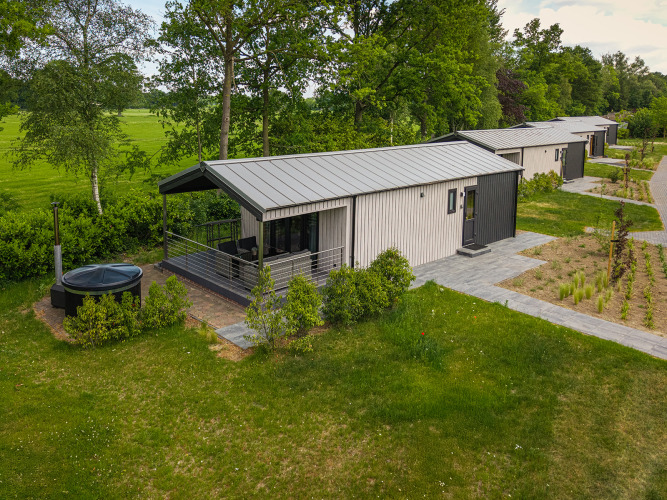 Terrassen-Lodge mit Sauna und Whirlpool im Holiday Resort 't Schuttenbelt in den Niederlanden, umgeben von Grün.