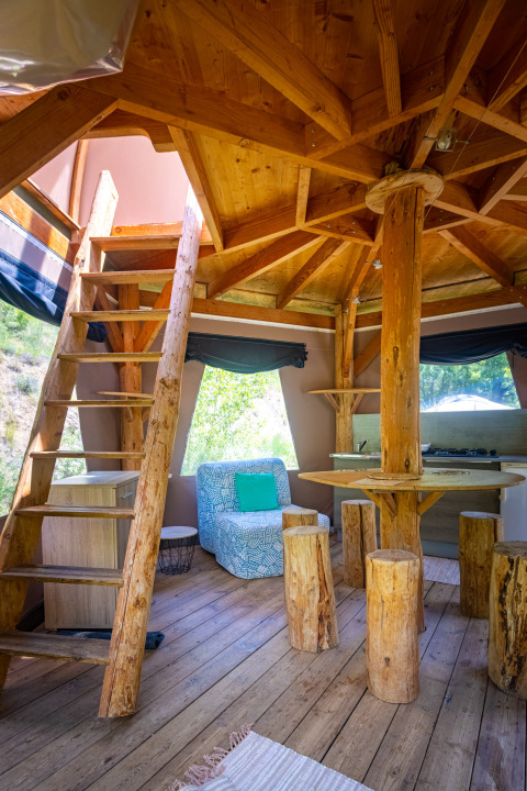 Binnenaanzicht van een uniek tipi-tent met rustieke houten meubels en trap bij Camping Des Randonneurs.