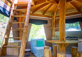 Vista interna di una tenda tipì unica con arredi rustici in legno e scala al Camping Des Randonneurs in Francia.