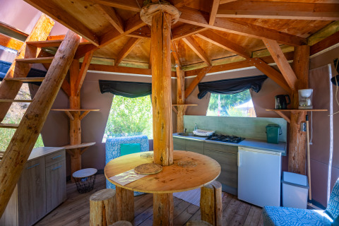 Interieur van een unieke tipi-tent met keuken en houten meubilair bij Camping Des Randonneurs in Frankrijk.