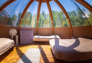 Interno di un moderno teepee a bolla con tre letti, grandi finestre e vista sulla foresta in Francia.