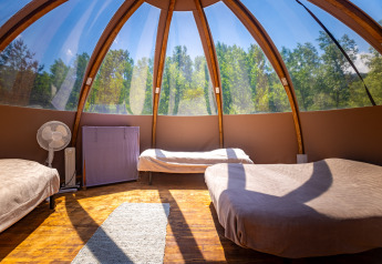Interior de una tipi burbuja moderna con tres camas, grandes ventanales y vistas al bosque en Francia.
