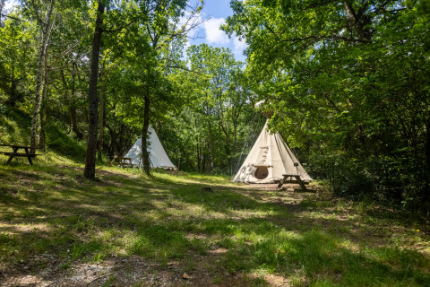 Dos tiendas tipi sin baño en Camping Des Randonneurs en Francia, rodeadas de árboles y bancos de picnic.