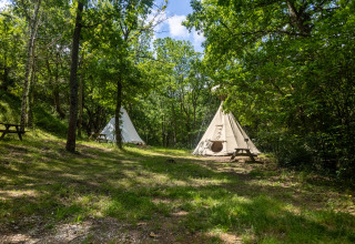 Dos tiendas tipi sin baño en Camping Des Randonneurs en Francia, rodeadas de árboles y bancos de picnic.