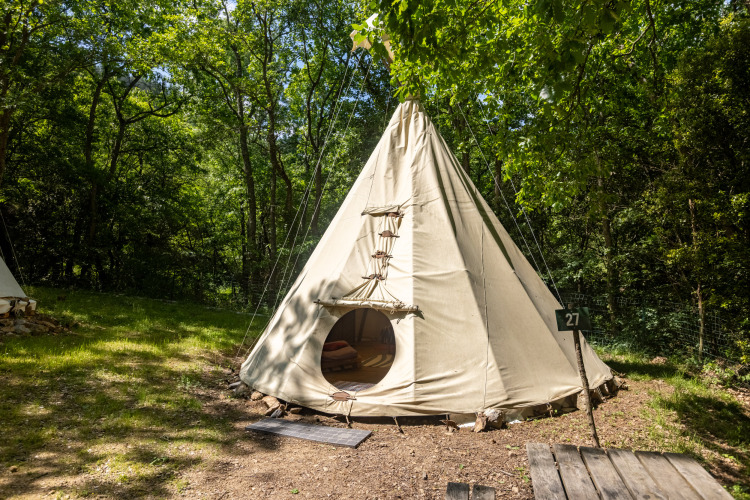 Tienda tipi llamada 'Tipi - sin baños' en Camping Des Randonneurs, rodeada de bosque verde en Francia.