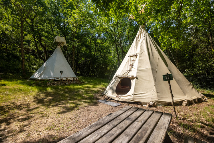 Dos tiendas tipi en Camping Des Randonneurs, Francia, situadas entre árboles y mesa, sin aseos incluidos.