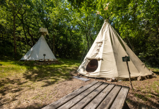 Dos tiendas tipi en Camping Des Randonneurs, Francia, situadas entre árboles y mesa, sin aseos incluidos.