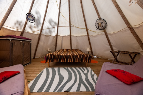 Interior de tipi con cama doble, camas individuales, decoración rústica y suelo de madera en camping francés.