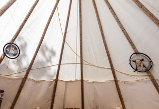 Vista interior de una tienda tipi con estructura de madera, cama doble y lámparas en Camping Des Randonneurs en Francia.