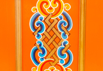 Traditionelles mongolisches Muster auf einer orangen Jurtenwand mit blauen und gelben Details.