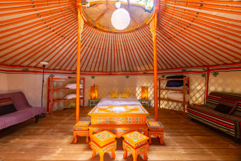 Interior of a colorful traditional yurt at Camping des Randonneurs - Yurts Occitanië with wooden floors and décor.