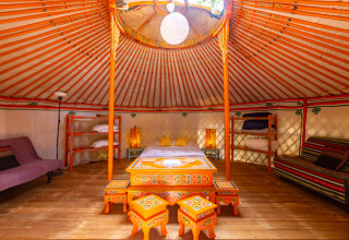 Indretning af en luksuriøs, farverig mongolsk jurte på Camping des Randonneurs - Yurts Occitanië med træmøbler.