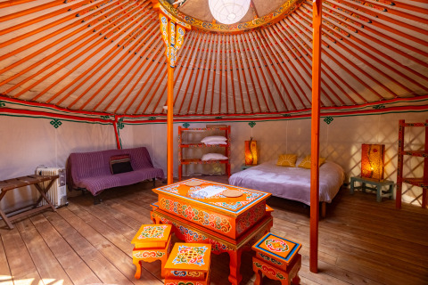 Interieur van een traditionele yurt met kleurrijk beschilderde meubels, bed, sfeerverlichting en houten vloer.