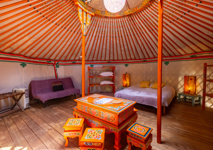 Interieur van een traditionele yurt met kleurrijk beschilderde meubels, bed, sfeerverlichting en houten vloer.