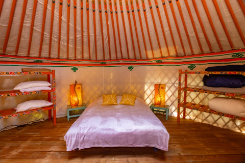 Interno accogliente di yurta al Camping des Randonneurs con letto matrimoniale, scaffali e lanterne.