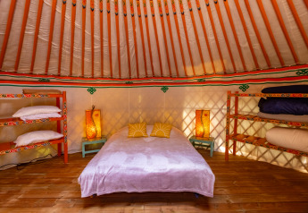 Cozy yurt interior at Camping des Randonneurs with double bed, colorful shelves and lanterns decor.