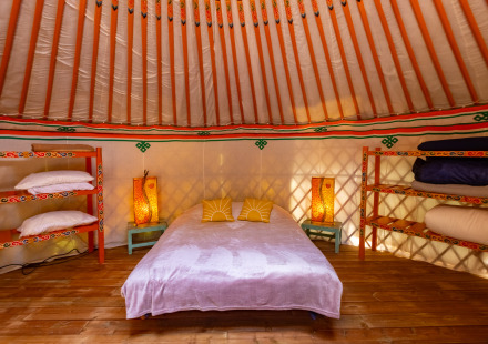 Gezellige yurt bij Camping des Randonneurs met tweepersoonsbed, kleurrijke planken en sfeerlampen.