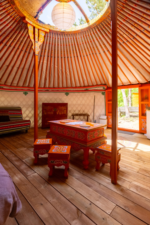 Indvendig udsigt af en traditionel mongolsk yurt med farverigt møbler og naturligt lys fra ovenlysvinduet.