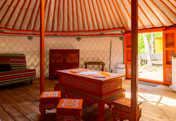 Vista interior de una yurta tradicional con muebles coloridos pintados, suelo de madera y luz natural arriba.