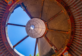 Uitzicht omhoog door de versierde dakopening van een traditionele joert met blauwe lucht erbuiten.