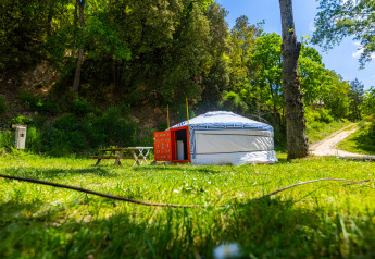 A traditional yurt used for glamping at Camping des Randonneurs, set in a green forest clearing with benches.