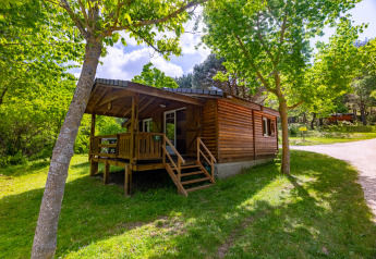 Wooden chalet with covered porch nestled among green trees at Camping Des Randonneurs in France in summer.