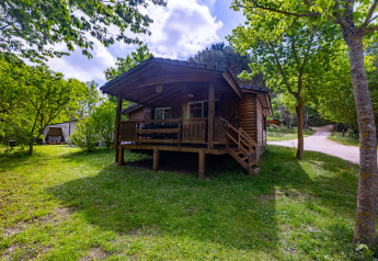 Wooden chalet at Camping Des Randonneurs in France, nestled among green trees and sunlit grassy area.
