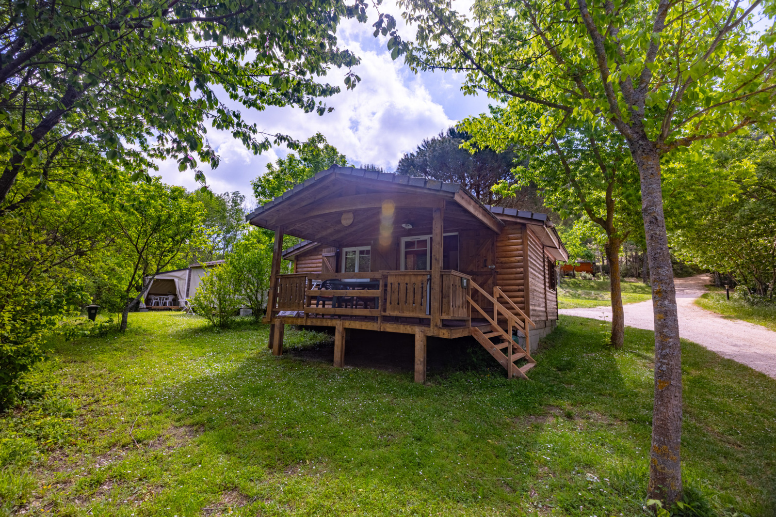 Houten chalet met veranda omgeven door bomen bij Camping Des Randonneurs in Frankrijk op een zonnige dag.