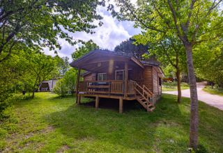 Wooden chalet with a front porch surrounded by trees at Camping Des Randonneurs in France on a sunny day.