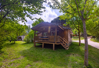 Chalet in legno con veranda circondato da alberi al Camping Des Randonneurs in Francia in una giornata di sole.
