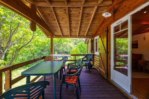 Covered wooden terrace at Chalet at Camping Des Randonneurs in France, surrounded by lush greenery.