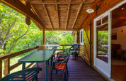 Covered wooden terrace at Chalet at Camping Des Randonneurs in France, surrounded by lush greenery.